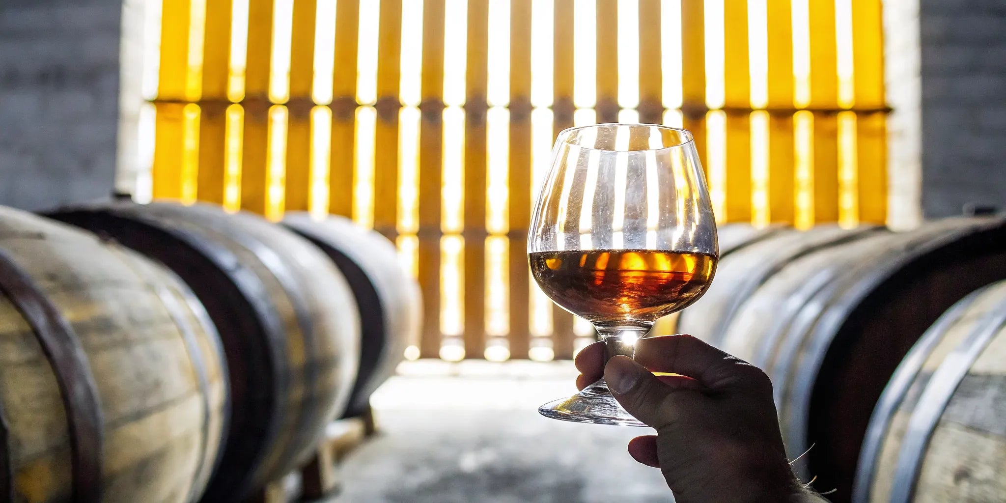 Pouring amber extra anejo tequila into a crystal tasting glass in a warm barrel warehouse