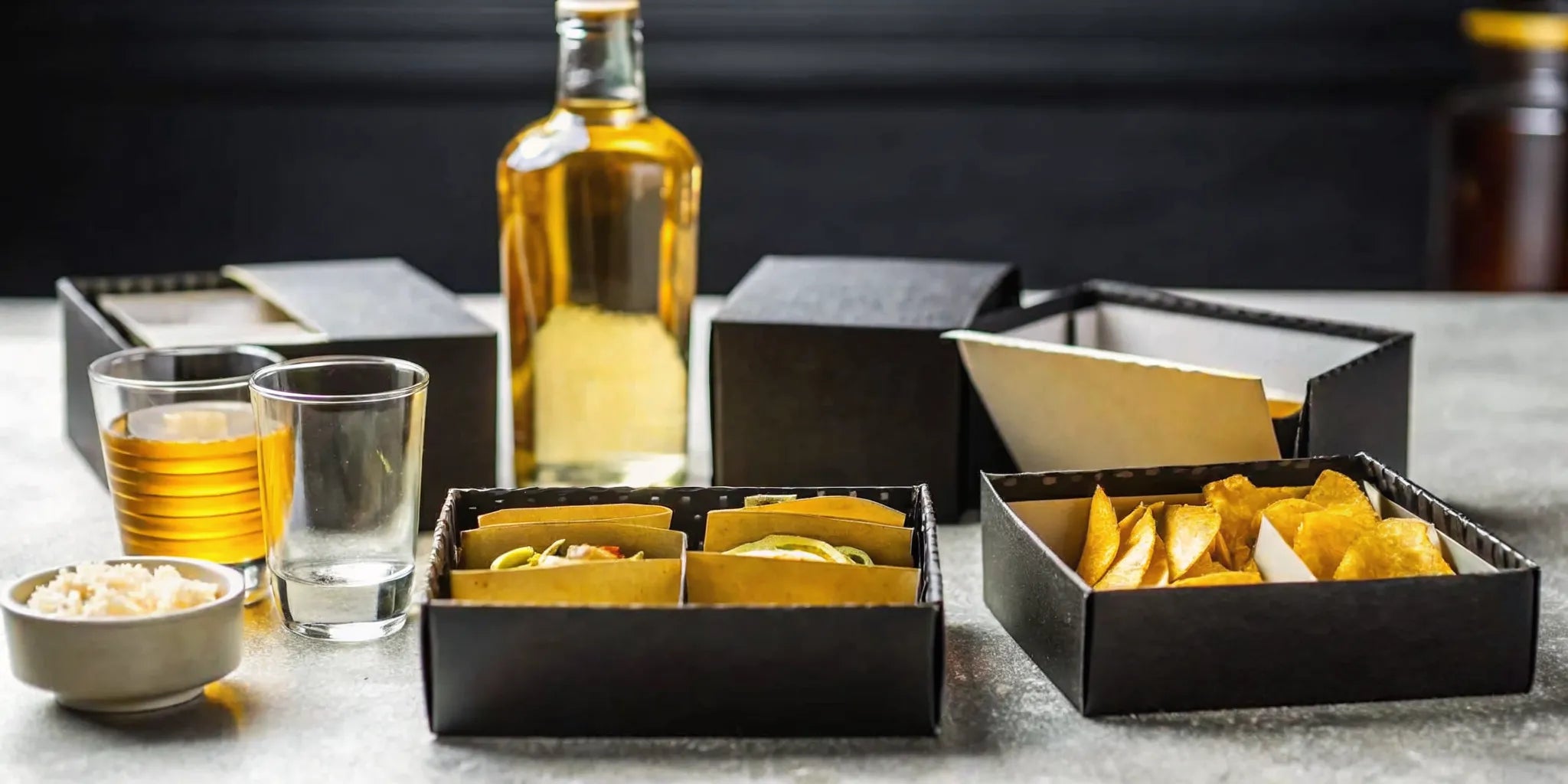 A monthly tequila box with a bottle of tequila, tasting glasses, and snacks.