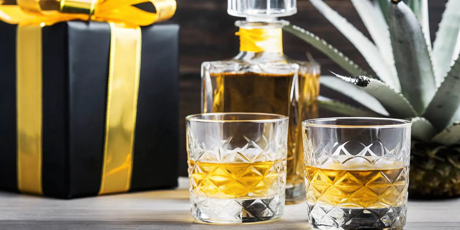 Elegant tequila gift arrangement on wooden table with premium bottle, ribbon, tasting glasses, and agave decor