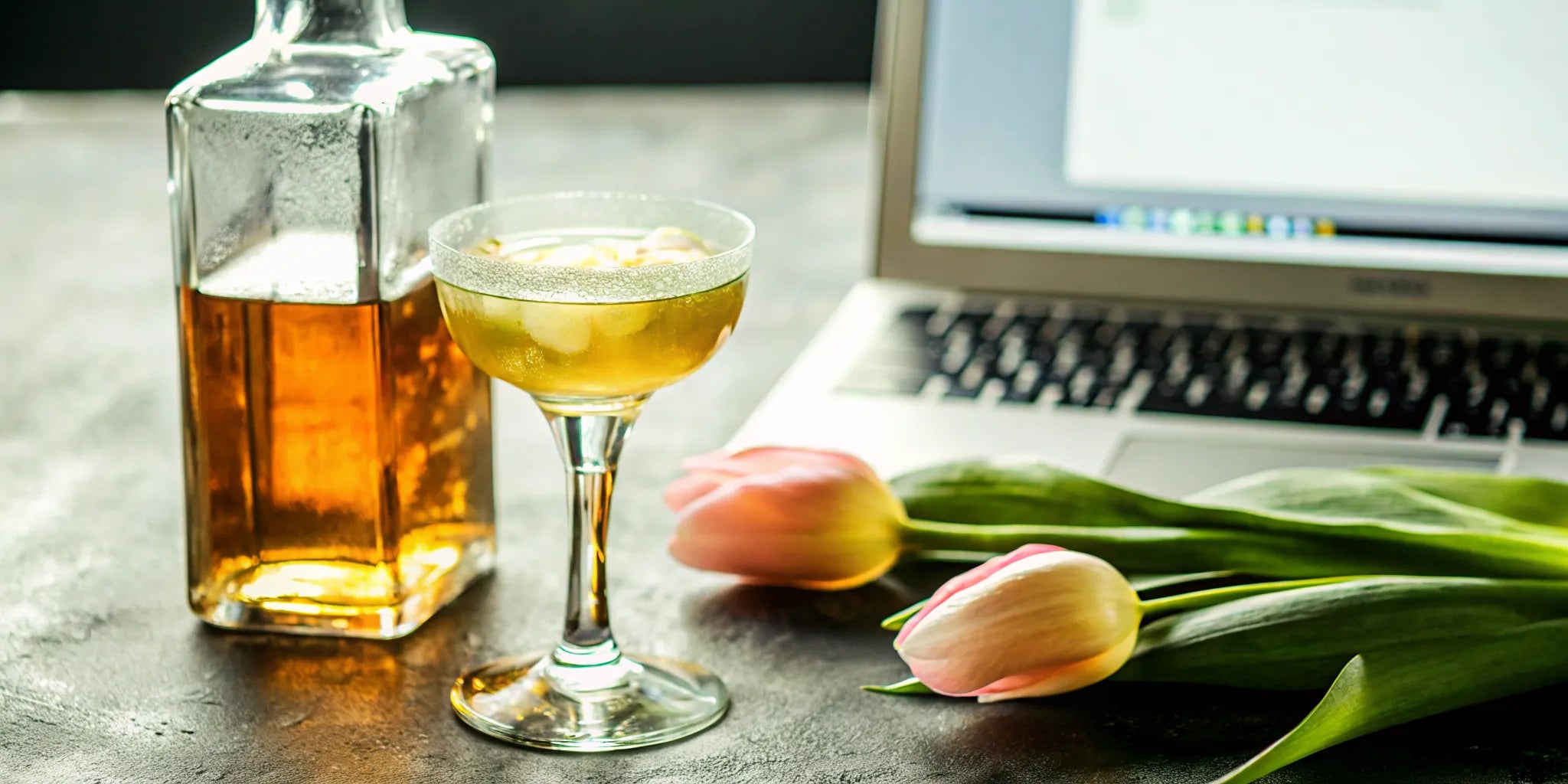 A glass of extra añejo tequila sits by a laptop, ready to buy a bottle online.
